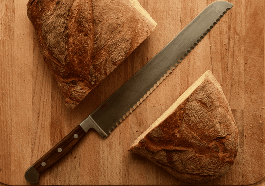 Serrated bread knife on a wooden board beside bread slices