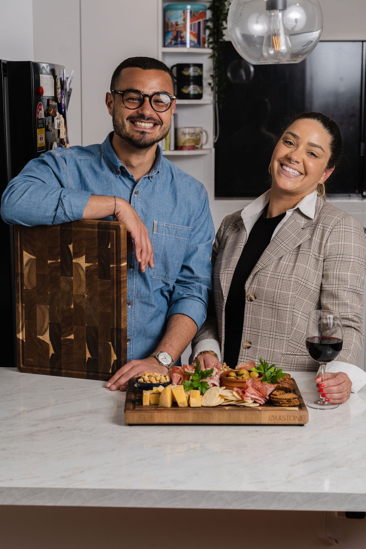 Couple with wine glasses beside a wooden board of food in a kitchen